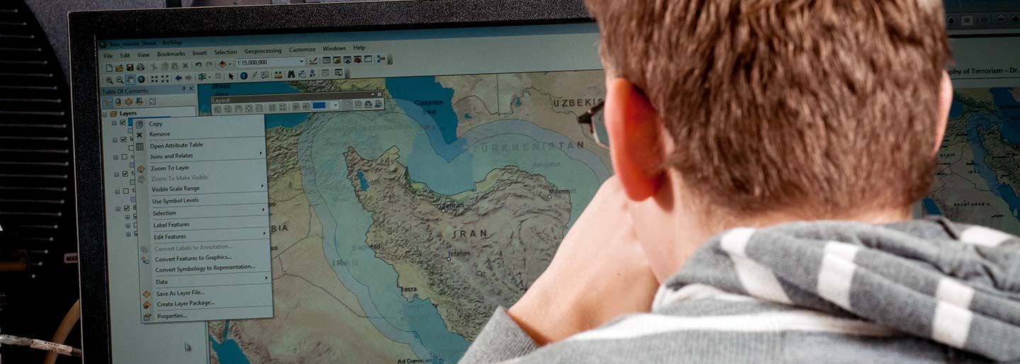 Student at a computer, inspecting a map of Iran.